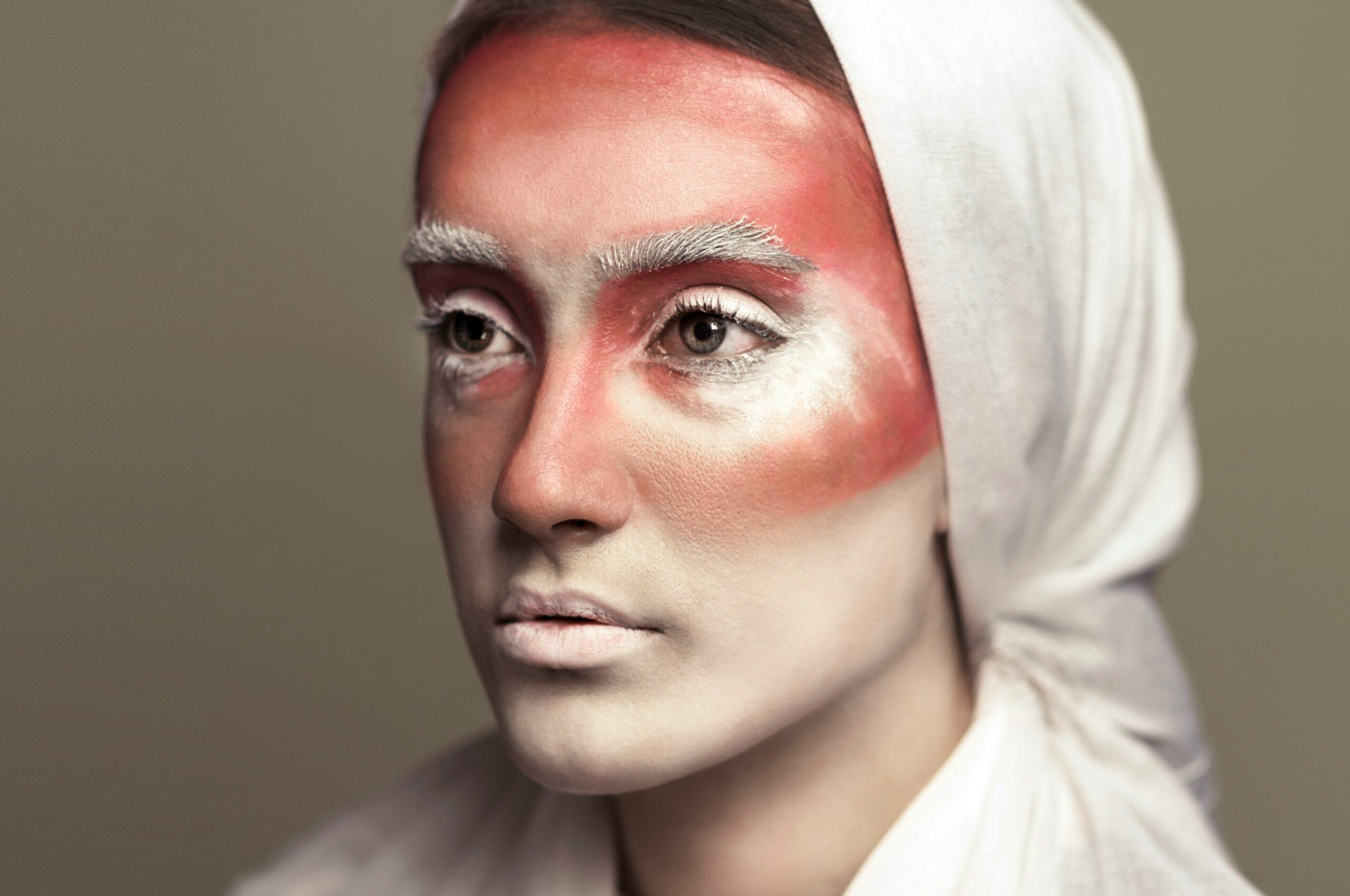 Model wearing avant garde geometric makeup with sharp angles and bold red hues